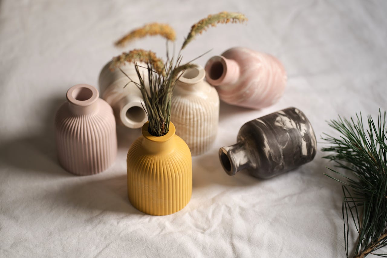 A collection of colorful ceramic vases elegantly arranged with a delicate floral accent on a soft white background.